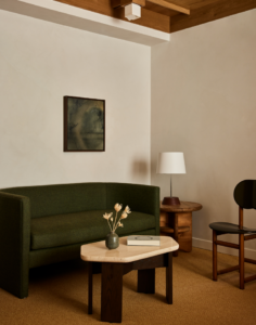 Maharam fabric wrapped green sofa, small coffee table made of travertine and wood, and an end table with a lamp, at our Aspen luxury hotel.