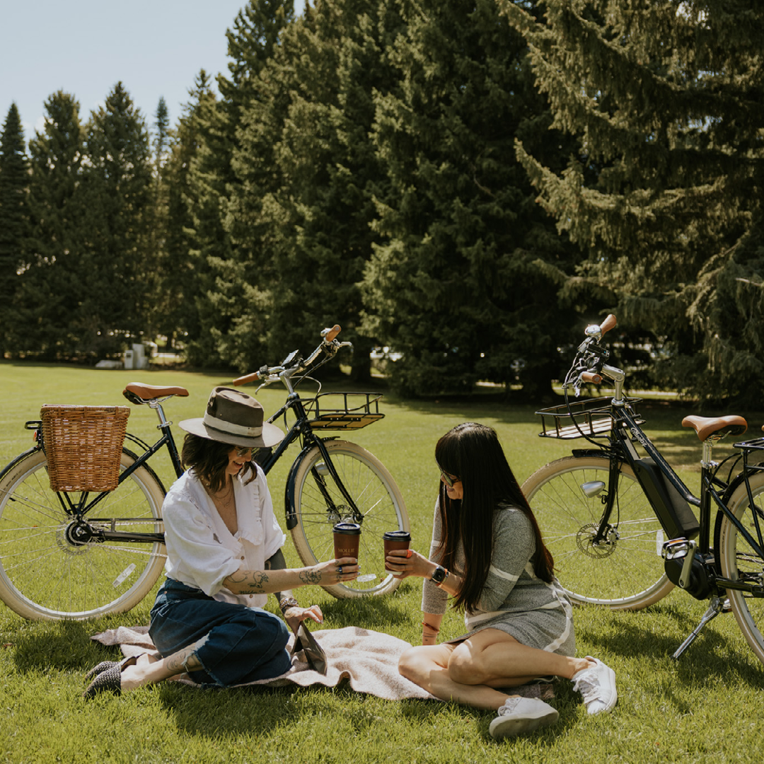 Two women with coffee cups, sitting on a picnic blanket with two bikes behind them near our hotel in downtown Aspen.