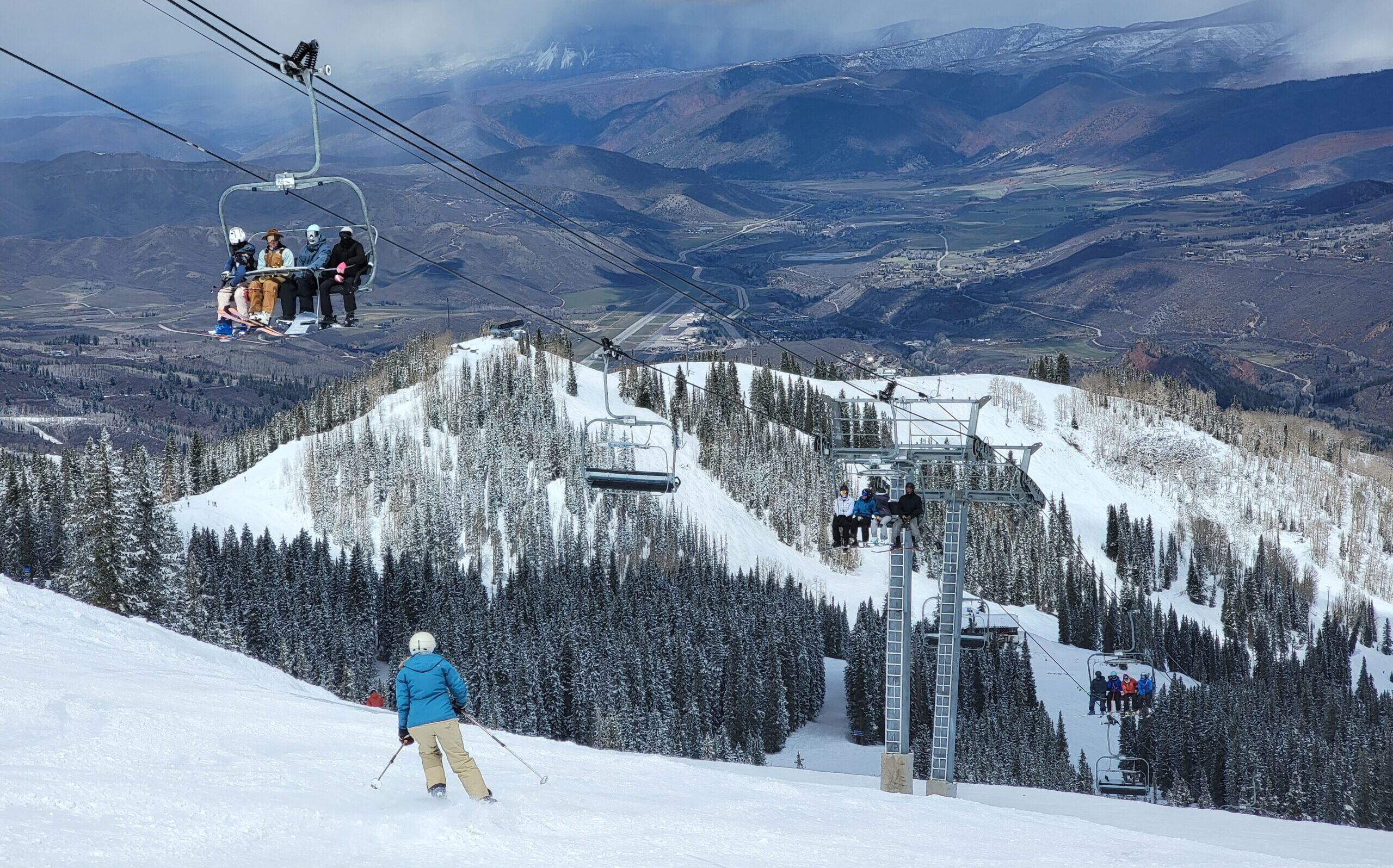 Skiers on a chairlift watching someone ski below them