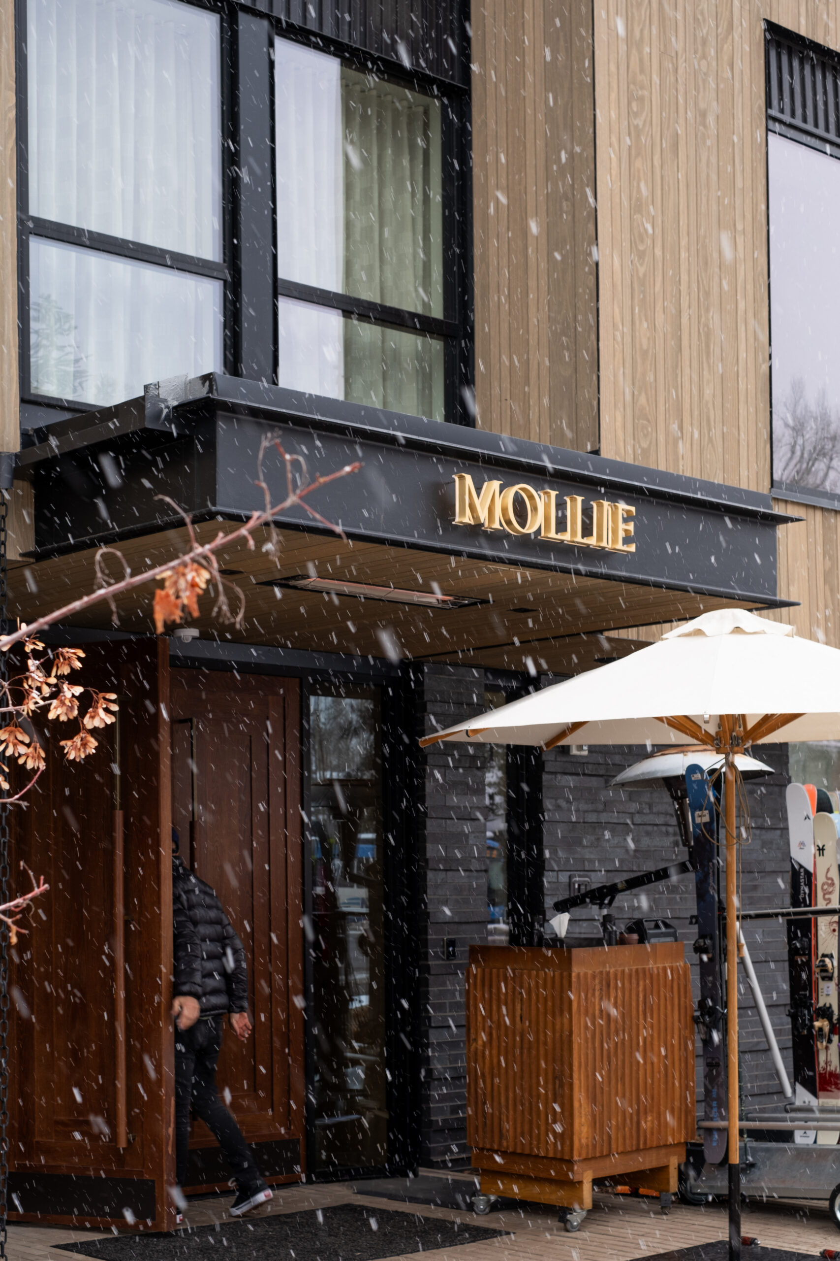 Snow falling past the MOLLIE gold sign at the hotel entrance in Aspen, Colorado